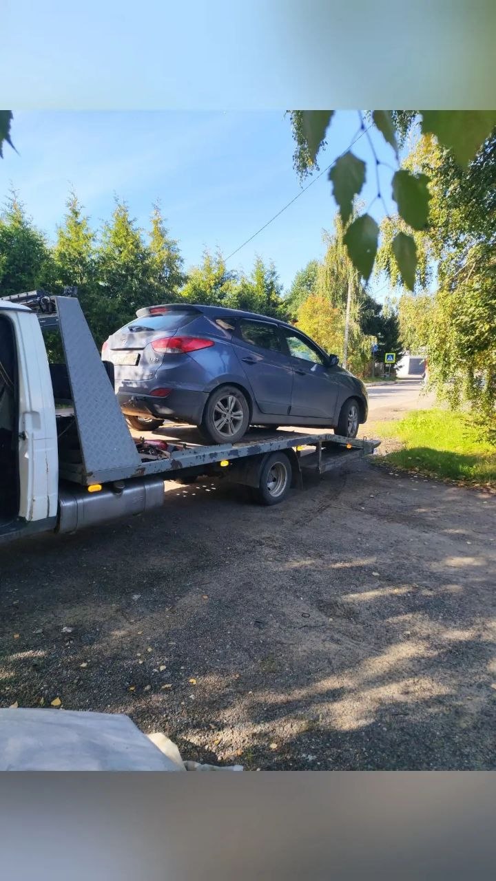 Эвакуатор везёт легковой автомобиль по трассе на рассвете