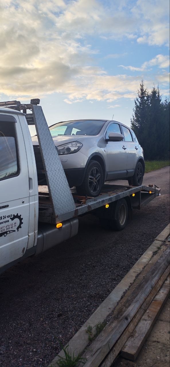 Эвакуатор везёт легковой автомобиль по трассе на рассвете