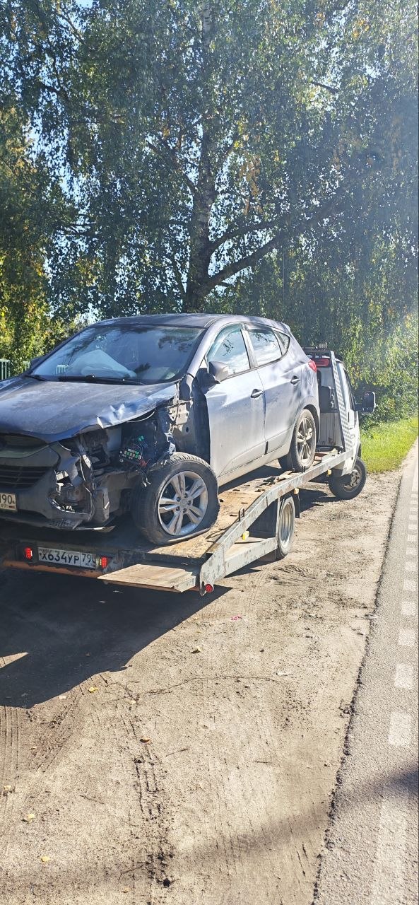Эвакуатор везёт легковой автомобиль по трассе на рассвете
